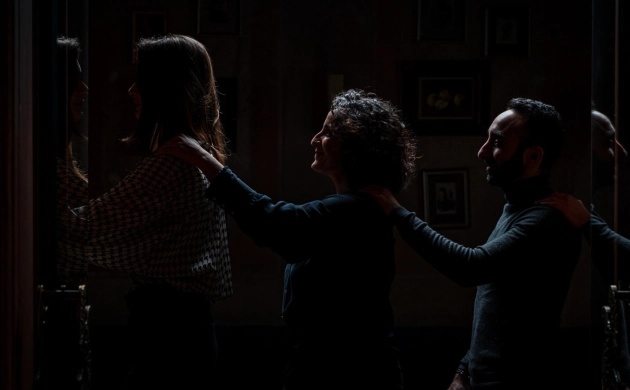 Trois personnes avancent en file indienne dans l'obscurité, posant leurs mains sur les épaules de la personne devant elles, guidées dans une expérience sensorielle immersive.