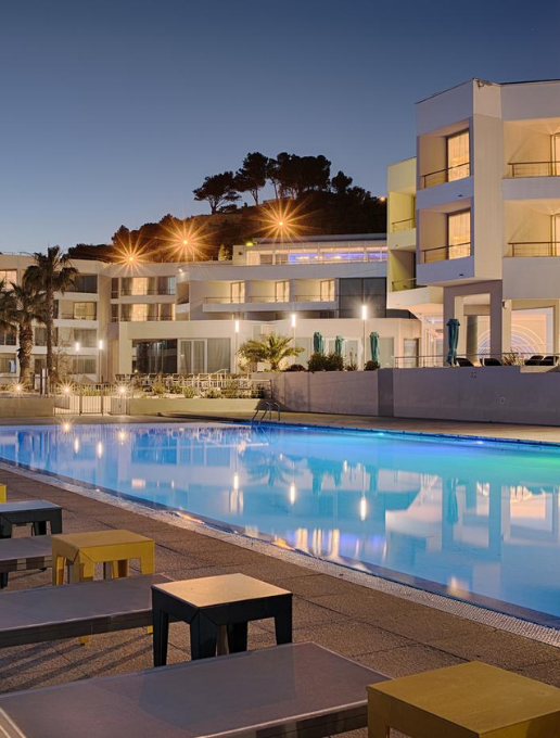 View of the nhow Marseille at dusk, with its large illuminated swimming pool and modern buildings in the background.