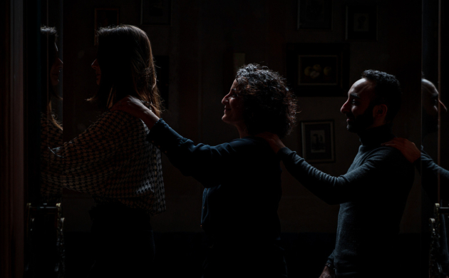 Trois personnes avancent en file indienne dans l'obscurité, posant leurs mains sur les épaules de la personne devant elles, guidées dans une expérience sensorielle immersive.