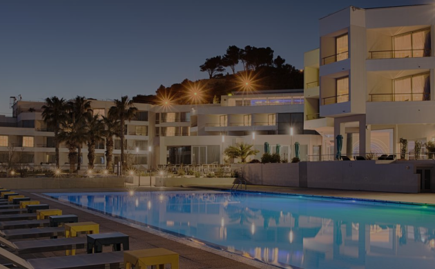 Hôtel nhow Marseille éclairé de nuit, avec grande piscine, chaises longues et palmiers en bord de mer.