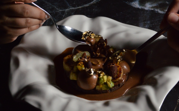 Dessert gastronomique au chocolat dressé dans une assiette blanche ondulée, dégusté à la cuillère, avec touches dorées et morceaux de fruits